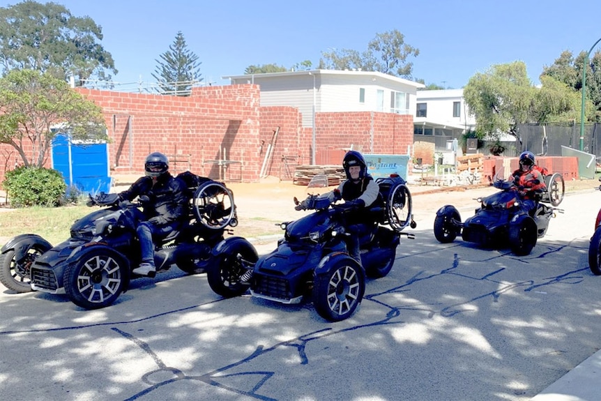 Four men sit on adapted trikes wearing helmets in the shade