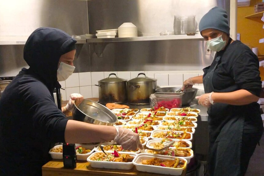 Women in masks preparing food in restaurant kitchen.