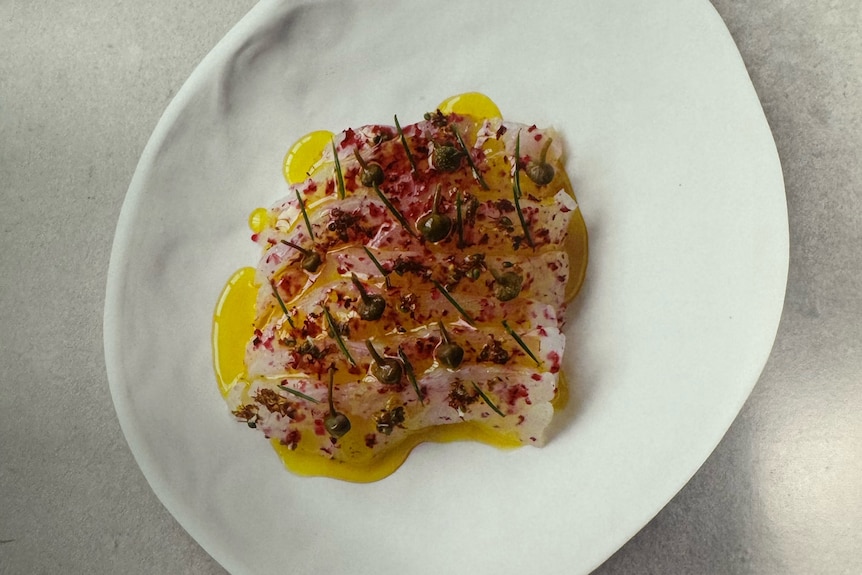 un plato blanco con trucha cubierta de aceite de oliva y alcaparras. 