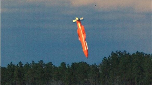 An orange coloured GBU-43 bomb is about to land in an empty paddock.