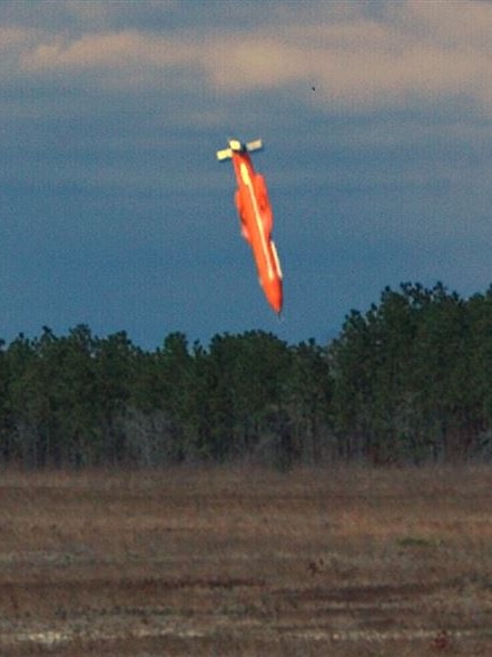 An orange coloured GBU-43 bomb is about to land in an empty paddock.