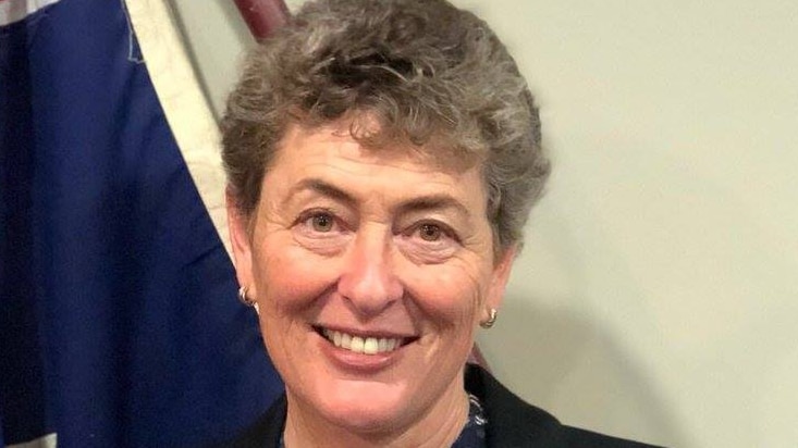 a woman in a black suit jacket standing in front of the Australian flag