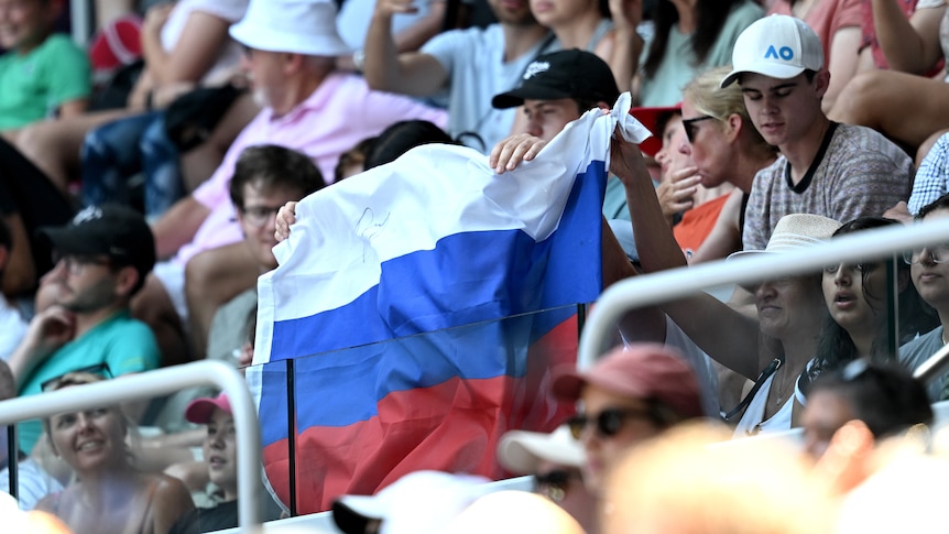 Fans hold up a Russian flag during an Australian Open tennis match between Andrey Rublev and Dominic Thiem.