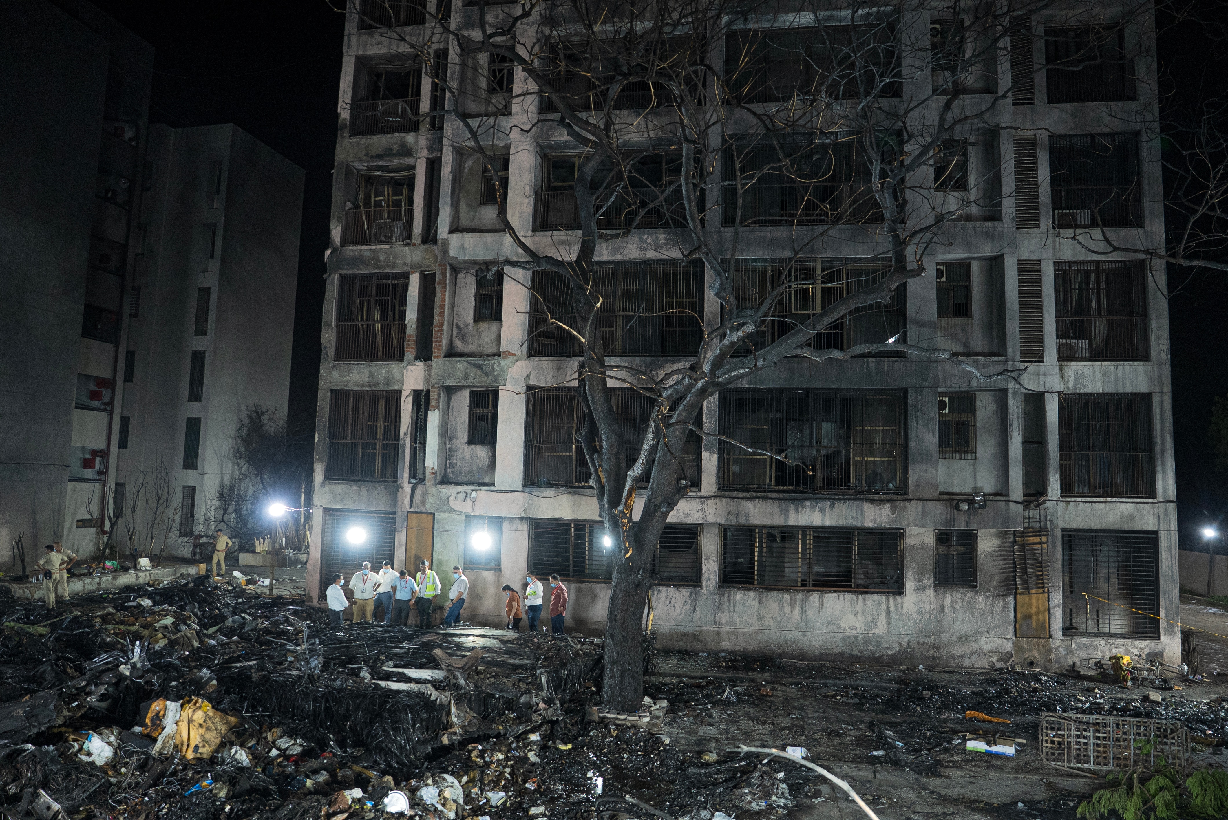 A burned out building and tree, with several people standing nearby.