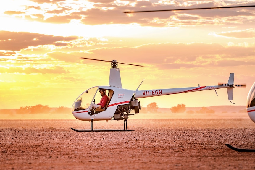 a helicopter sitting on a dusty outback plain at sunset