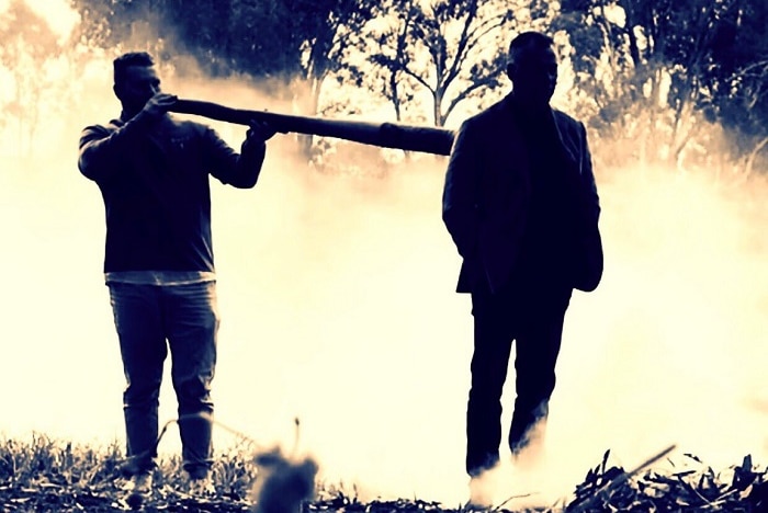 two aboriginal men standing in the bush surrounded by ceremonial smoke