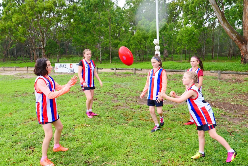 Five sisters playing footy together, wearing red, blue and white striped football jumper.