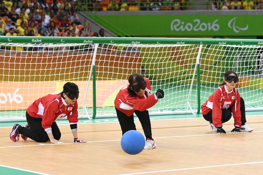 A goalball player wearing eyeshades hurls the ball down the court during a game at the Rio Paralympics.