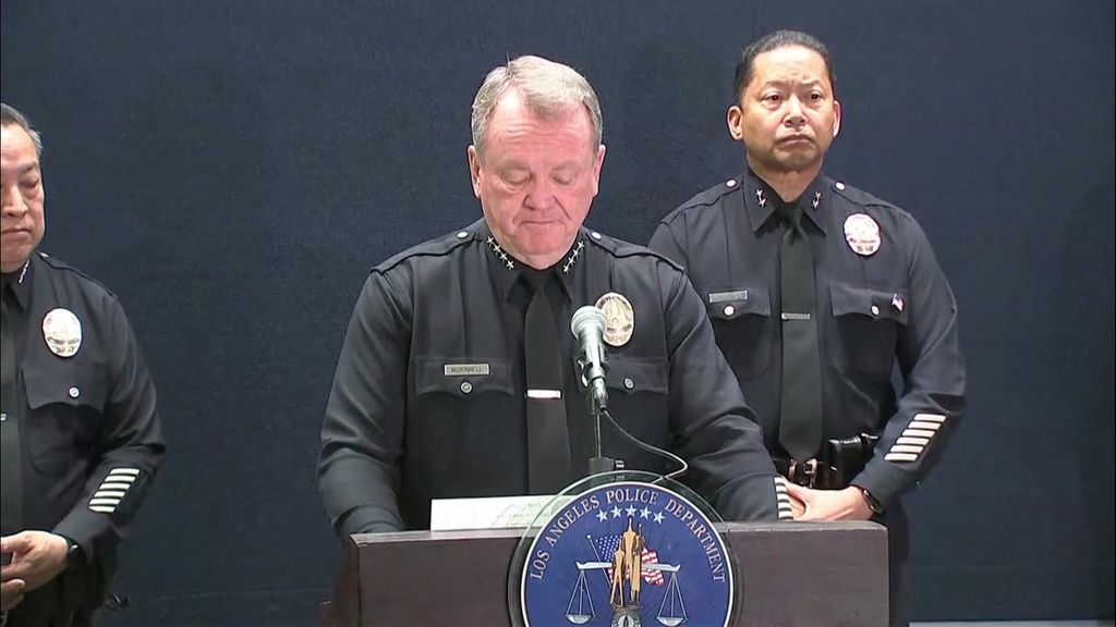 A police officer stands at a lectern speaking with two police officers on either side of him.