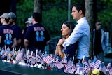 A fiance holds a woman from behind as she stands near a memorial to her father. 