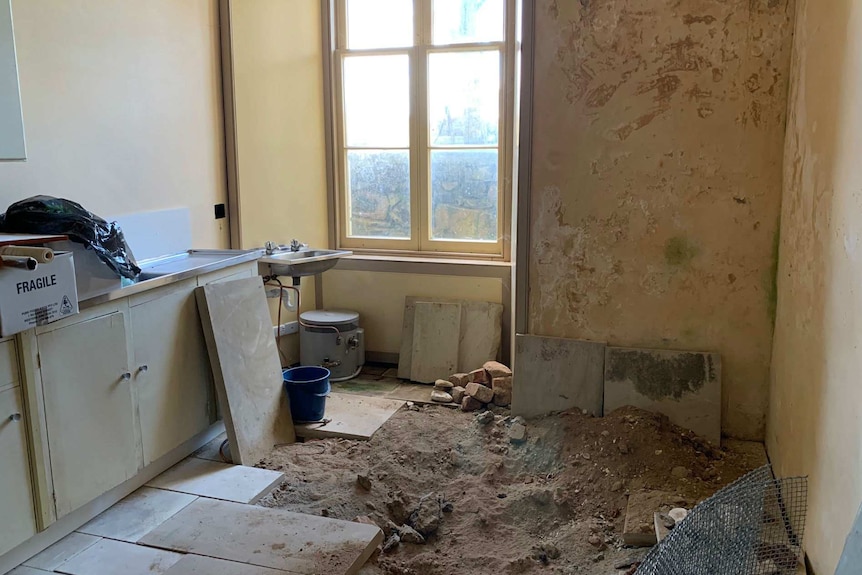 Large slabs of a floor are pulled up, exposing dirt, inside a historic home