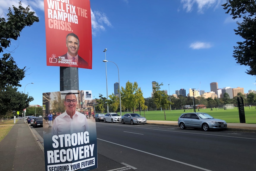 Two election posters on a stobie pole showing Peter Malinauskas and Steven Marshall. In the background is the city skyline
