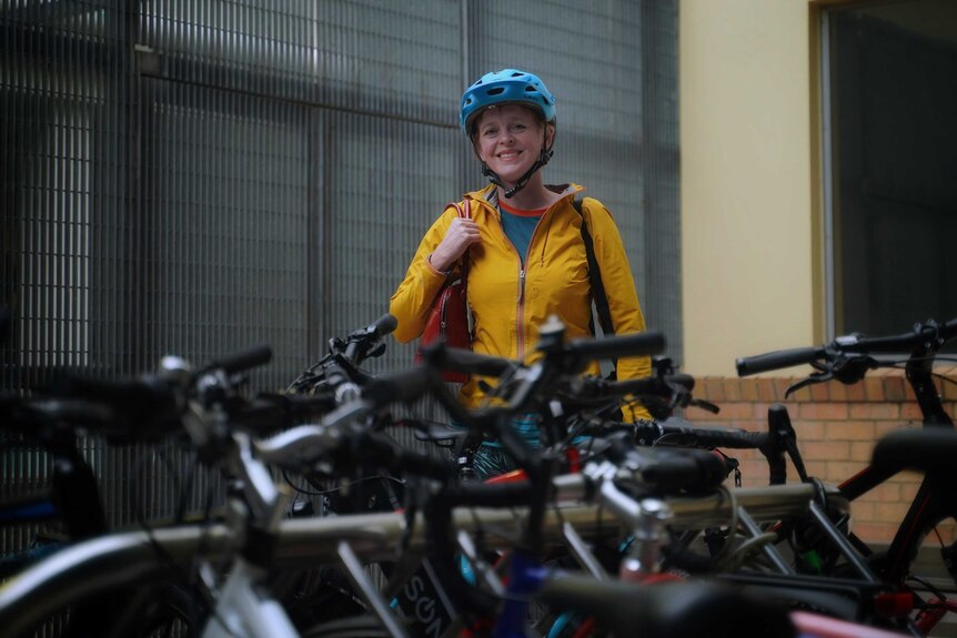 A woman in a yellow jacket and blue cycling helmet stands behind lots of bicyles.