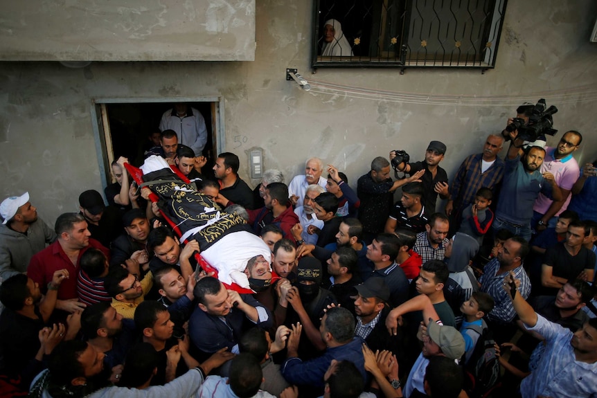 Crowd of mourners carry the body of a Palestinian militant through a narrow street in Central Gaza.