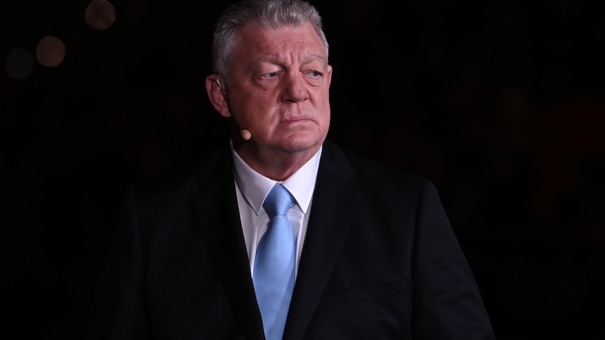 Commentator Phil Gould in a suit, with a microphone, doing a broadcast for television