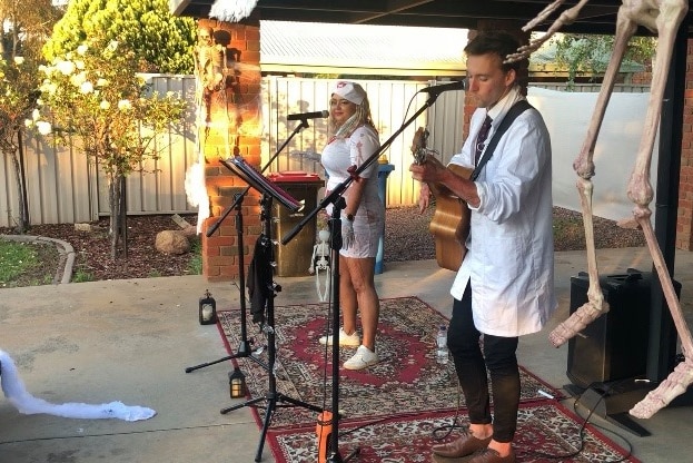 A female singer and a male guitarist playing music on a driveway.