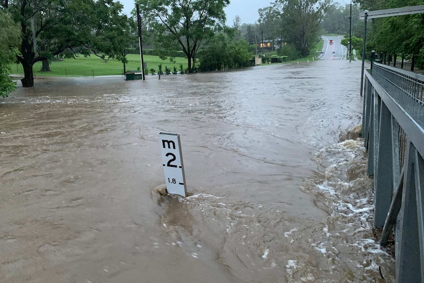 Floodwaters cover a road. A flood marker juts out of the brown water, the water is up to 1.7 metres.