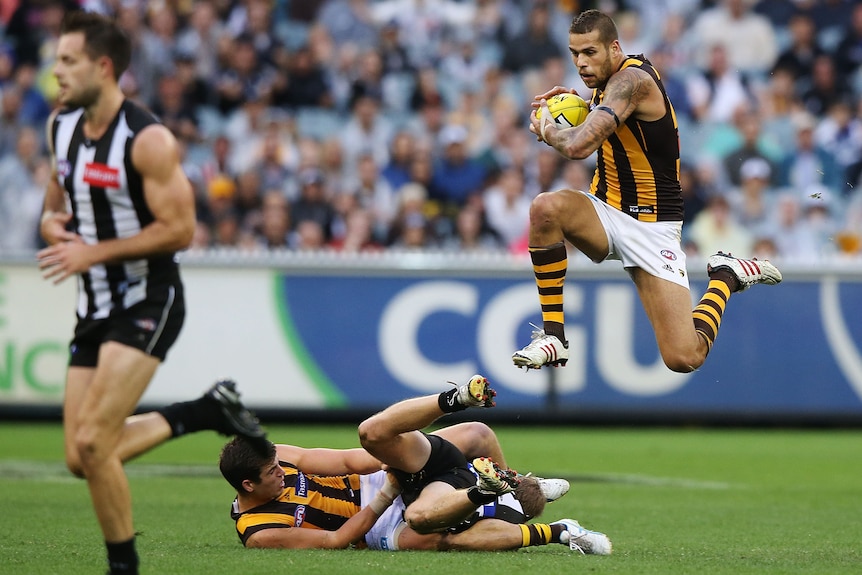 Lance Franklin hurdles some players laying on the ground while he carries the ball