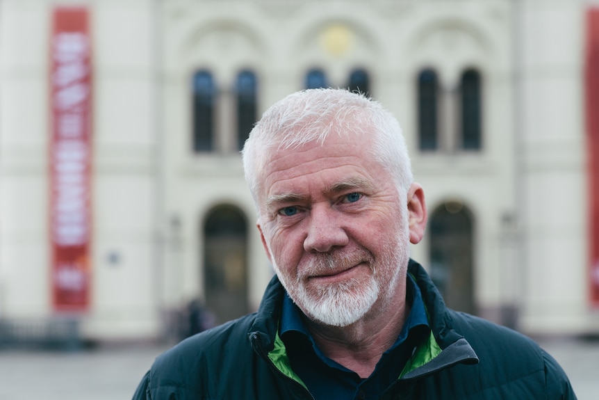 A closeup of a man with white hair looking at the camera. 