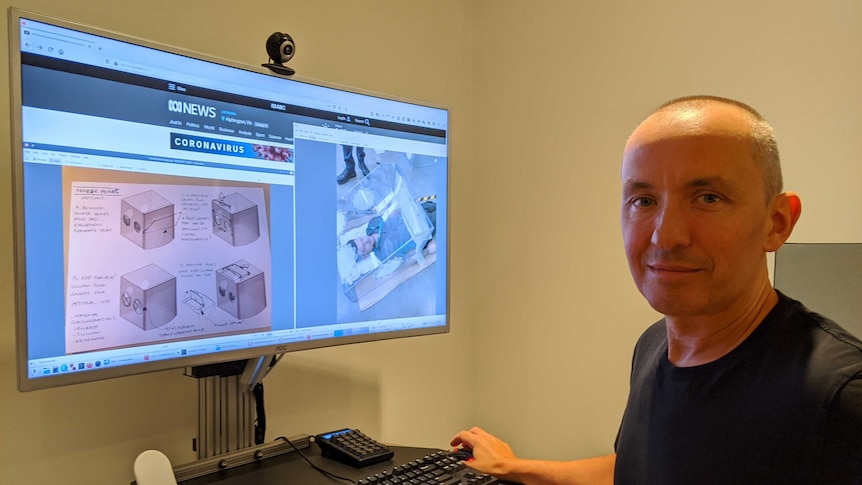 A man in front of a computer screen with a prototype on it, smiling at camera.