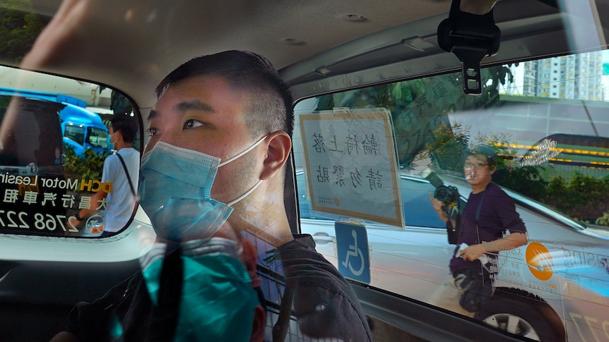 A man wearing a face mask sits in the back of a car