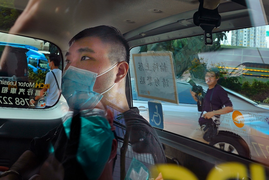 A man wearing a face mask sits in the back of a car