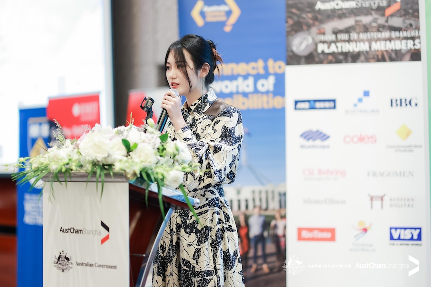 A woman in a floral dress speaking into a microphone.