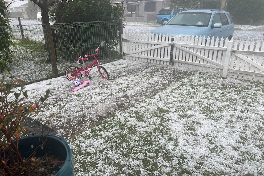 Hail stones cover a front yard with a small kids bike in it
