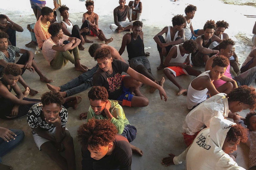 A group of Libyan migrants who were rescued from the sunken boats sit on the ground