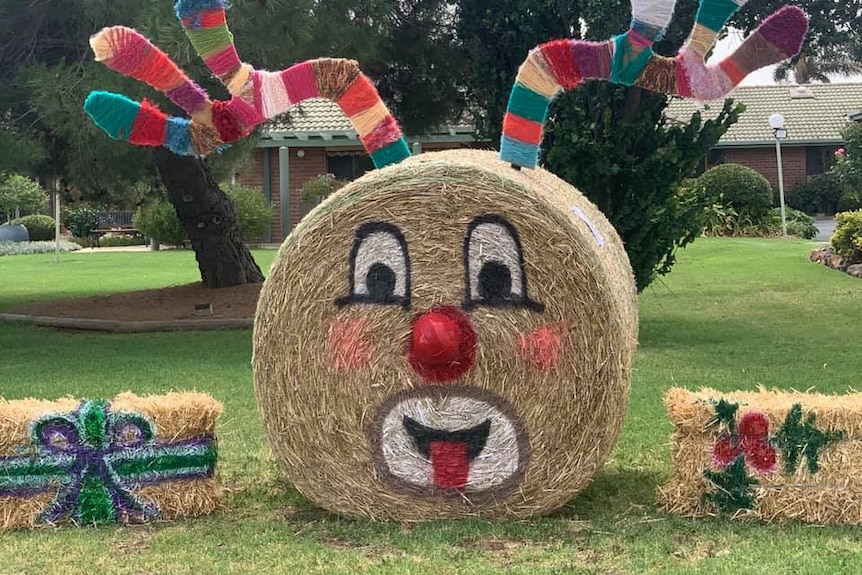 small square hay bales painted like wrapped presents next to large hay bale painted like Rudolf