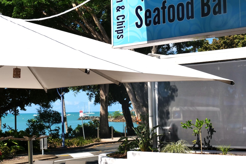 a sign that says 'seafood bar' in the top right with airlie beach in the background.