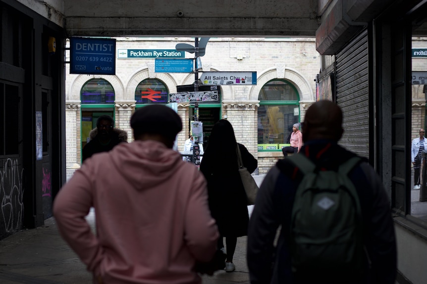 A view through the exit of the Peckham tube station. People in hoodies exit into the street
