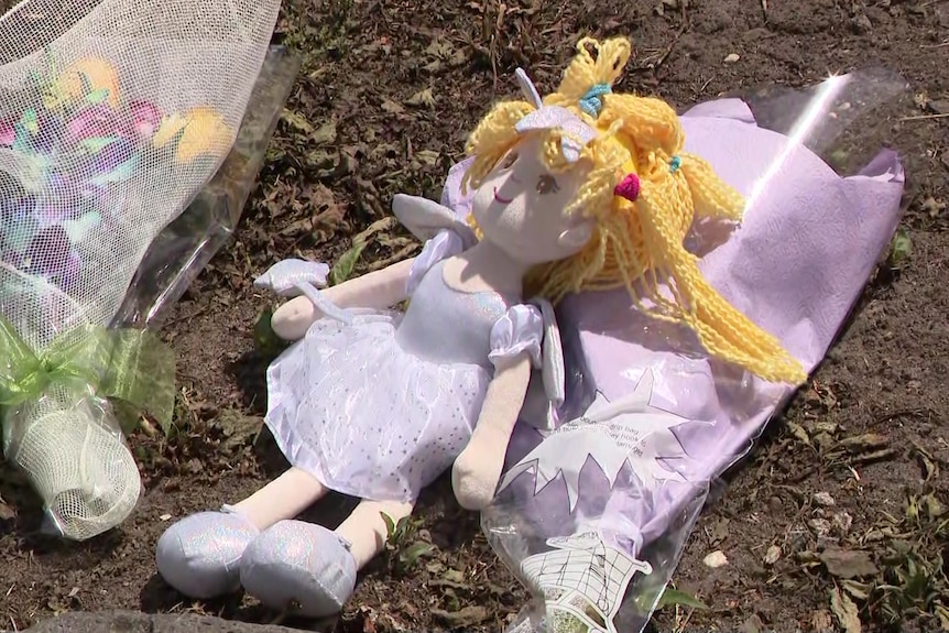 Two bunches of flowers sit on the ground with a doll
