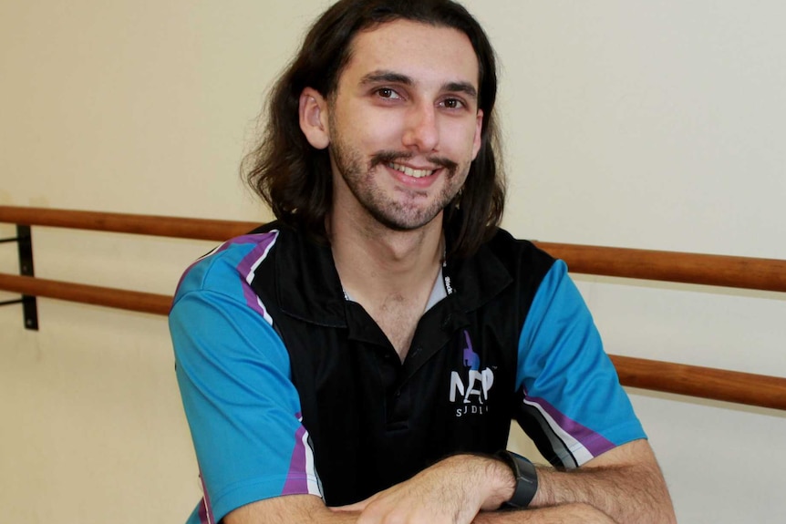 A man sits backwards on a chair in the middle of a dance studio