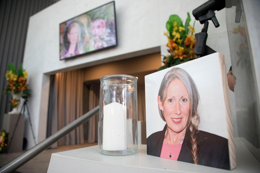 photo of a woman with her hair braided in a pony tail sits on a rise next to a candle in a jar with flowers and a screen behind