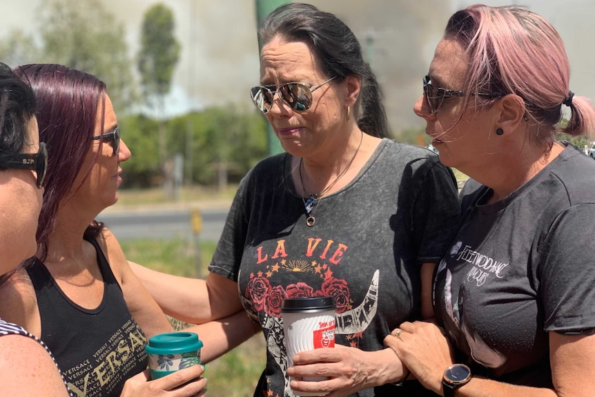 Faith Gordon, wearing aviator sunglasses and holding a coffee, is surrounded by three other women. She is welling up.