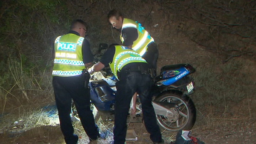 Police officers in yellow vests look at a motorcycle