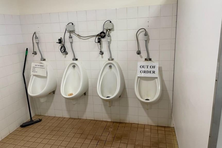 Dirty urinals with out of order signs hanging on two of them.