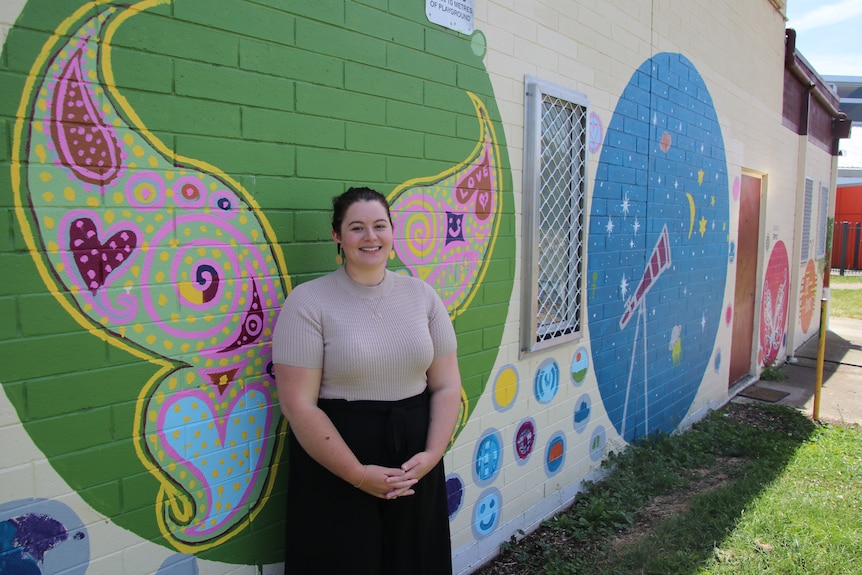 Taylor Bouvy stands in front of a wall with colourful murals.