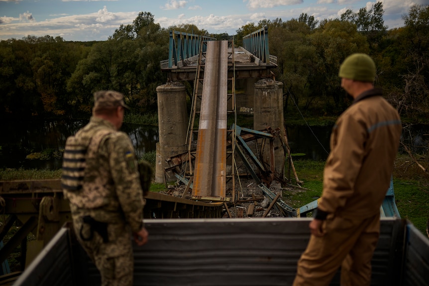 Ukrainian soldiers remove metal structure pieces as they work on a bridge damaged during fighting.
