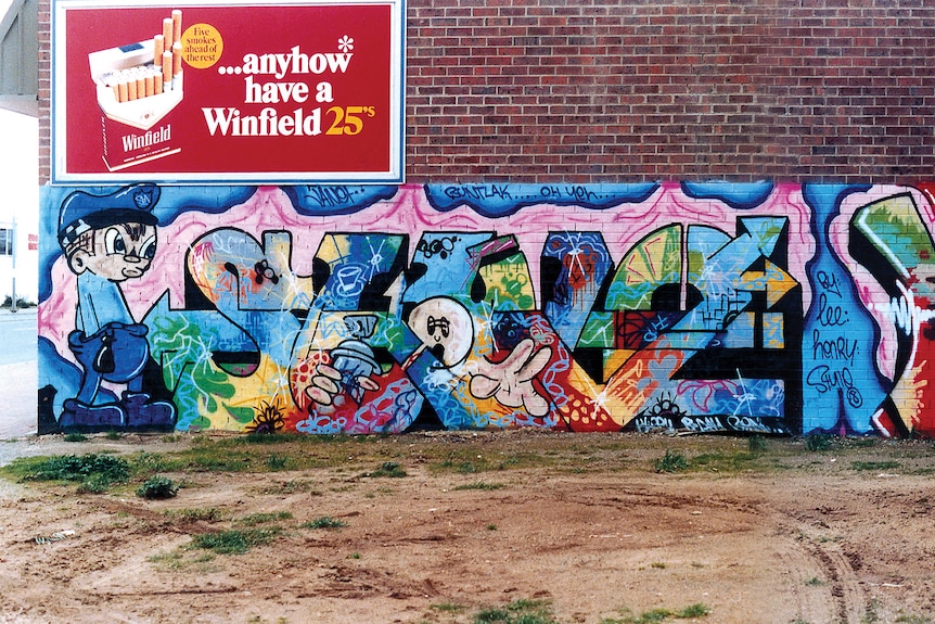 Colourful graffiti on a wall below a cigarette ad.