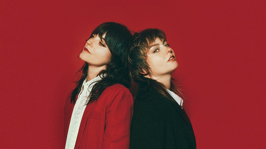 Sharon Van Etten and Angel Olsen stand back-to-back against a dark red background