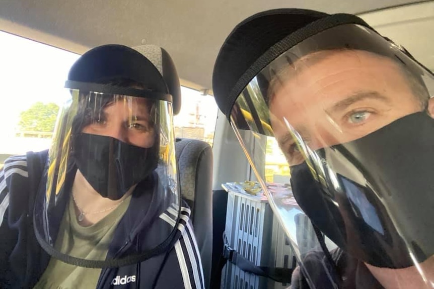 A man and a woman wearing face masks and shields.