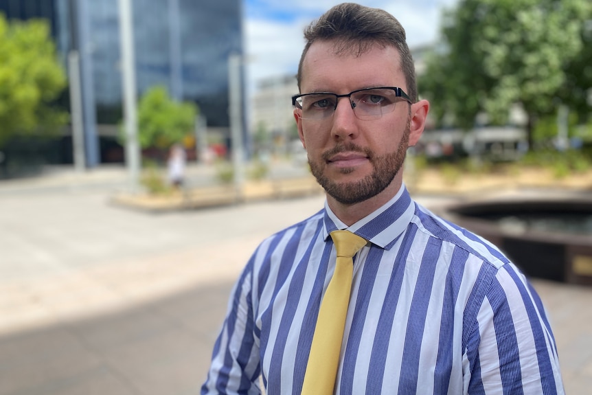 A man in a blue and white striped collared shirt looks serious.