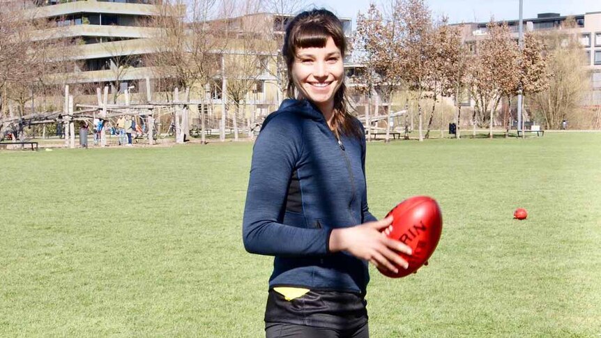 A young woman stands on an oval holding a football.
