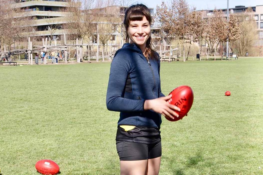 A young woman stands on an oval holding a football.