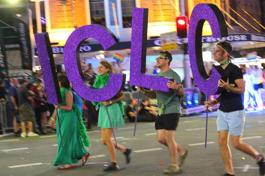 Four people parade at the Madi Gras, each holding large purple letters 'I', 'C', 'L', 'C'
