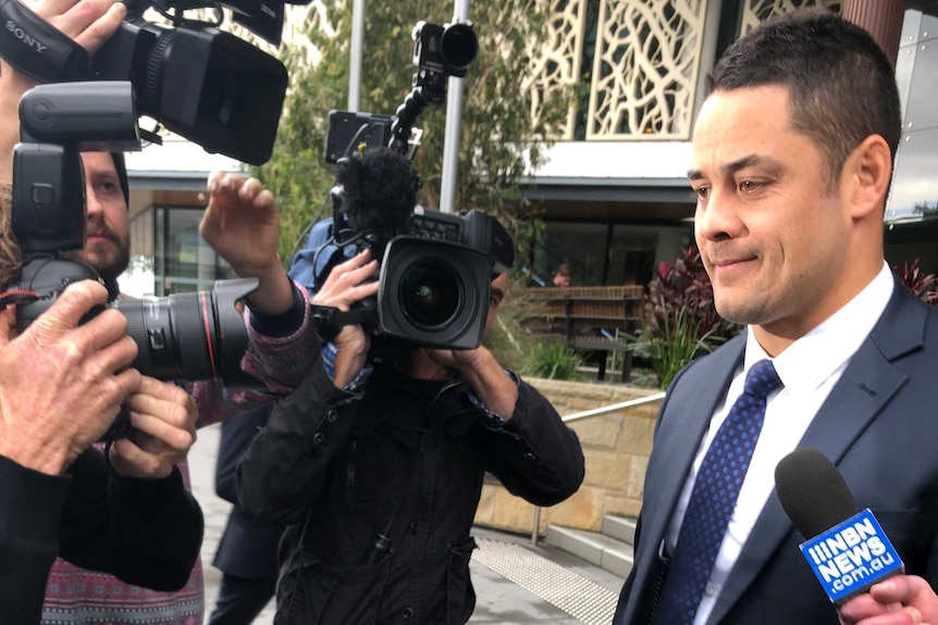 A man in a suit with short hair speaks to the media outside a court building.