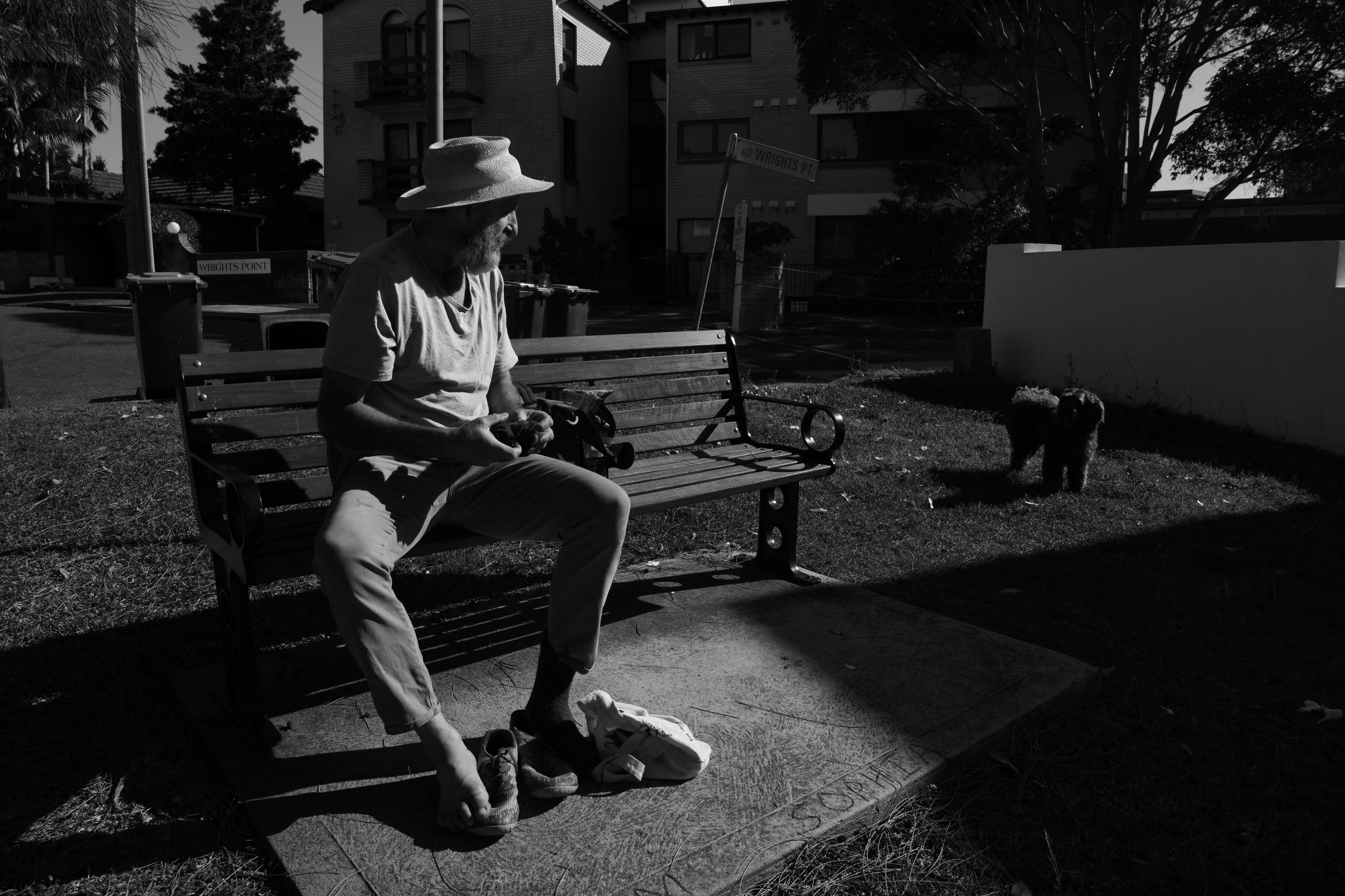 A man puts on shoes while sitting on a park bench