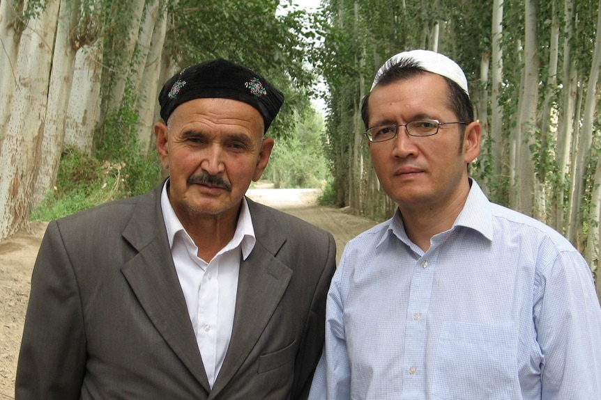 Two men with tress in the background wearing traditional Uyghur hats.
